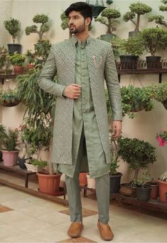 a man standing in front of potted plants wearing a green suit and brown shoes