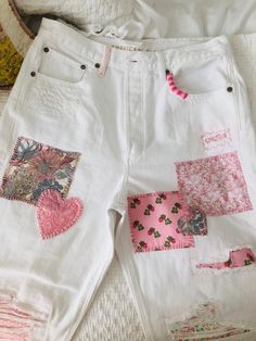 some white shorts with pink patches and hearts on the side are laying on a bed