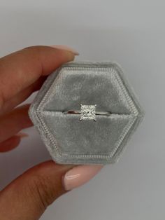 a woman's hand holding an engagement ring in a velvet box with the diamond setting on it