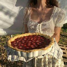 a woman holding a large pie on top of a table