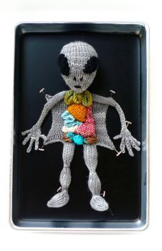 a small knitted figure is displayed on a black tray with silver trimmings