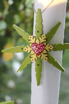 an ornament is hanging on the side of a pole with green leaves and a red heart