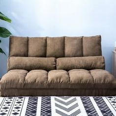 a brown futon couch sitting on top of a rug next to a potted plant