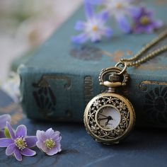 an antique pocket watch sitting on top of a book next to flowers and a chain