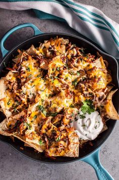 nachos in a skillet with sour cream and cilantro on the side