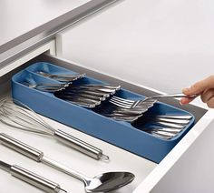 a person holding a knife and fork in a drawer with utensils on it