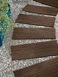 several pieces of wood sitting on top of gravel next to a planter filled with plants