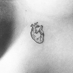 a small heart tattoo on the back of a woman's chest, it is black and white