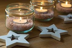 three mason jars filled with sand and lit candles sitting on top of a wooden table