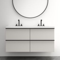 a bathroom vanity with two sinks and a round mirror on the wall above it, in front of a white wall