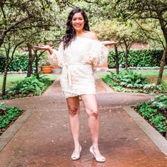 a woman in a white dress posing for the camera with trees and bushes behind her