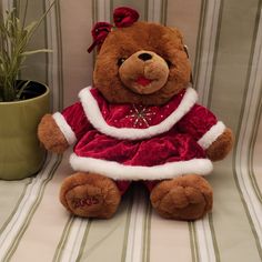 a brown teddy bear wearing a red dress sitting next to a potted plant