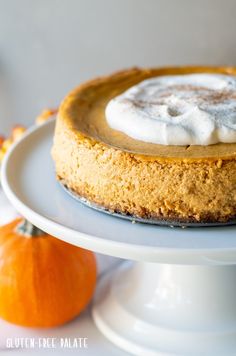 a pumpkin cheesecake with whipped cream on top sits on a white cake platter