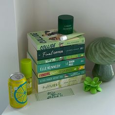 a stack of books sitting on top of a white table next to a green vase