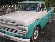 an old blue and white pickup truck parked in a parking lot next to a man