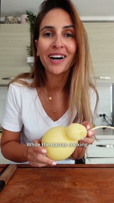 a woman holding an egg on top of a wooden table in front of a kitchen