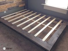 a bed frame made out of wood in a room with carpeted floor and walls