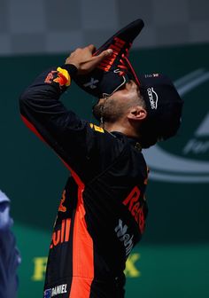 a man in black and orange is holding his hat up to his head while he stands on the sidelines