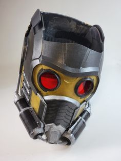 a close up of a mask on a white surface with red eyes and an iron man helmet