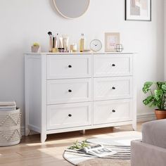 a white dresser sitting in a living room next to a mirror and potted plant