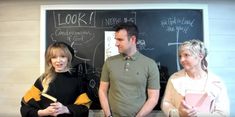 three people standing in front of a blackboard with writing on it and one person holding a folder