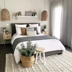 a bedroom with white and grey bedding, pillows and plants on the nightstands