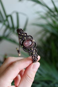 a hand holding a piece of jewelry in front of a plant