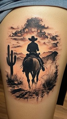 a woman with a cowboy tattoo on her thigh riding a horse in the desert at sunset