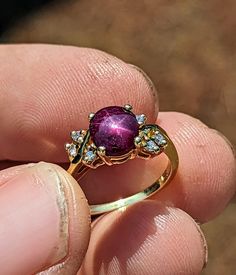 a close up of a person's hand holding a ring with a purple stone