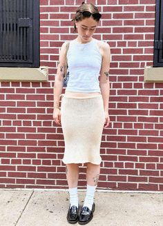 a woman standing in front of a brick wall wearing black shoes and a white tank top