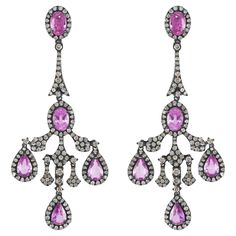 Drape yourself in the elegance of yesteryears with these Victorian 6.6 Cttw. Pink Sapphire and Diamond Chandelier Earrings. Each earring is a delicate confection of oval pink sapphires set in a diamond halo on a black rhodium surface, reminiscent of the intricate lacework that defined an era of sophistication. The surmount of the earring mirrors the connector, creating a seamless transition to the chandelier arms. These arms are a ballet of light and color, with round diamonds studded on black rhodium frames and pear sapphires in diamond halos that dangle with a regal air. The pièce de resistance is the final drop—a pear sapphire in a diamond halo—connected to the central arm, completing the chandelier's silhouette. Crafted with 8.4 grams of metal, these earrings are a testament to the gra Diamond Chandelier Earrings, Diamond Chandelier, Victorian Design, Seamless Transition, Black Rhodium, Gorgeous Jewelry, Dream Jewelry, Diamond Halo, Sapphire Diamond