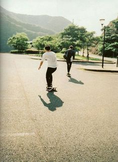 two skateboarders are riding down the street in front of some trees and mountains