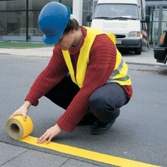 a woman wearing a hard hat kneels down to roll up yellow tape