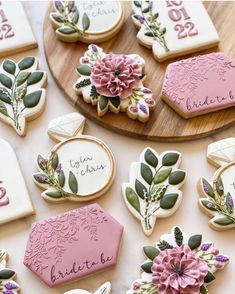 cookies decorated with flowers and leaves are on a wooden platter next to the names of bride and groom