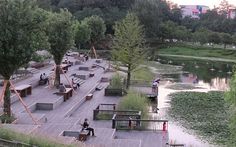 people are sitting on benches near the water and in the distance, there is a pond