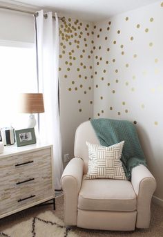 a white chair sitting in front of a window next to a wall with gold dots on it