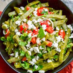 a black bowl filled with green beans, tomatoes and feta cheese on top of a red towel