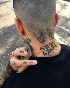 the back of a man's head with tattoos on his neck and hand in front of him