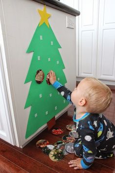 a toddler playing with a christmas tree made out of paper and magnets on the fridge