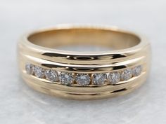 a gold wedding ring with five diamonds on it's sides, sitting on a white surface