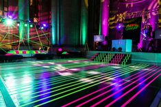 an indoor dance floor is lit up with colored lights and lines on the ground in front of a stage