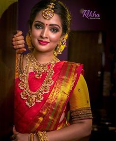 a woman in a red and yellow sari with gold jewelry on her neck, posing for