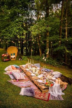 an outdoor dinner table set up in the middle of a forest with lights strung overhead