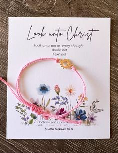 a pink cord bracelet with flowers on it and the words look up to christ written in gold