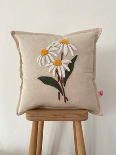 a white pillow with daisies on it sitting on a wooden stool next to a wall