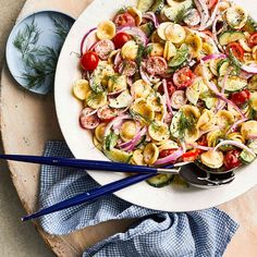 a white plate topped with pasta and veggies next to chopsticks on a wooden table