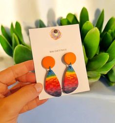 a pair of colorful earrings sitting on top of a white card next to a plant