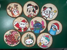 twelve wooden coasters decorated with cartoon characters on green table top next to red and white christmas tree ornament