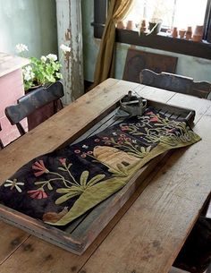 a wooden table topped with a tray filled with flowers and plants next to a window