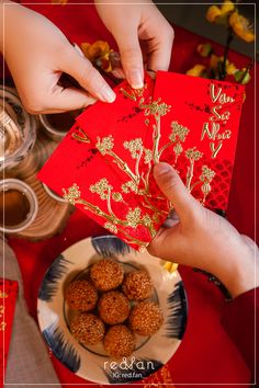 two hands holding red envelopes over a plate of food